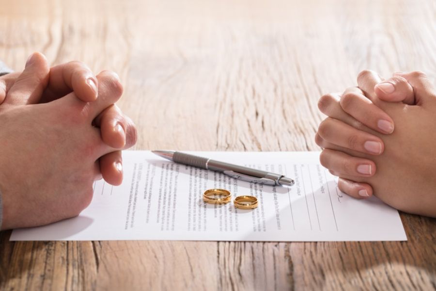 Ein Kugelschreiber und zwei Eheringe liegen auf einem Vertrag, während sich zwei Hände bei einem Anwalt für Familienrecht in Meppen gegenüber liegen. 
